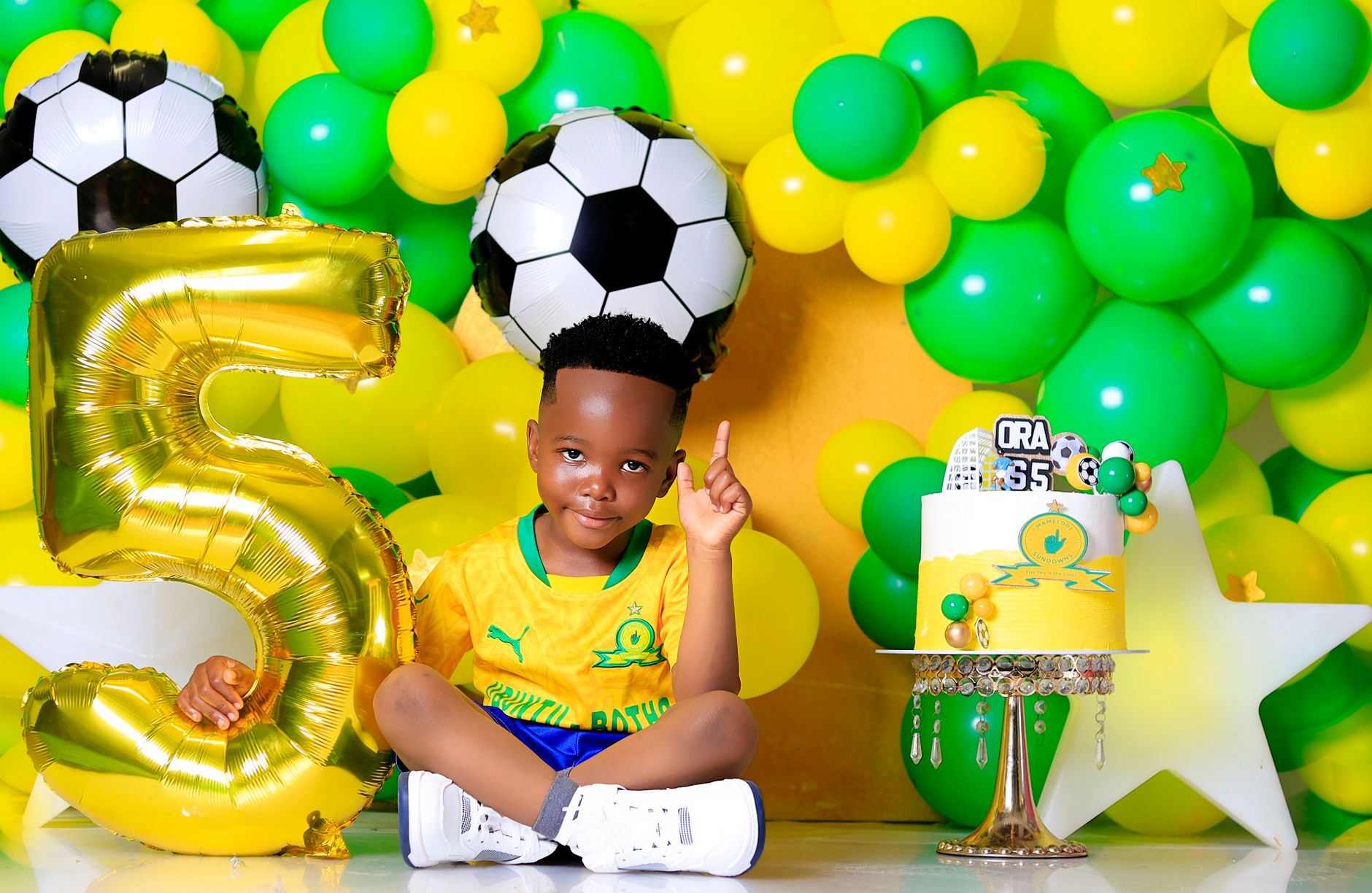 Young boy celebrating 5th birthday with soccer-themed decorations and cake.