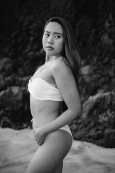 Striking beach portrait of a woman in a swimsuit with rocky background, in black and white.