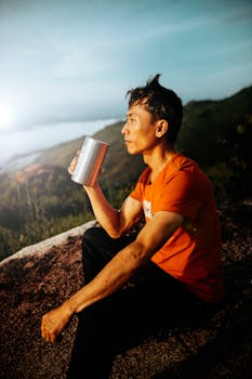 A man in an orange shirt enjoys a cup of coffee on a scenic hill in Kon Tum, Vietnam.