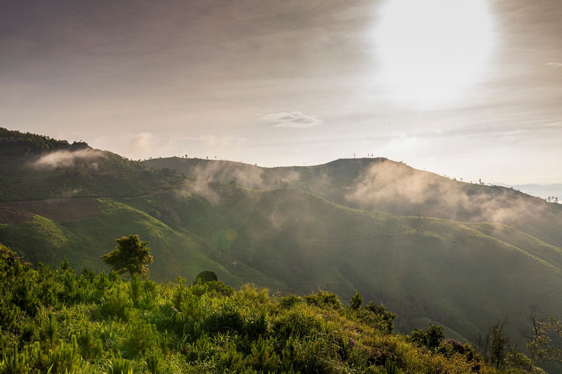 Dramatic sunrise over lush green mountains in Kon Tum, Vietnam, with misty clouds and bright sunlight.
