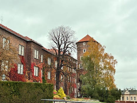 Wawel Castle in Kraków showcasing vibrant autumn foliage against a cloudy sky.