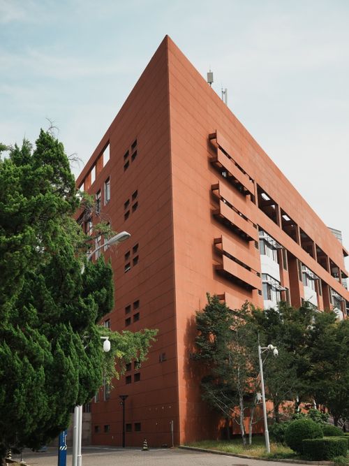 Free A striking red building with modern architectural design captured among greenery on a clear day. Stock Photo