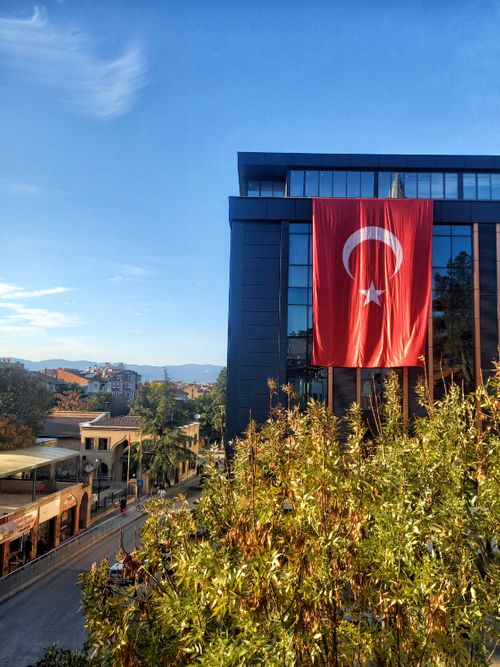 Free A large Turkish flag waves from a modern building in Burdur, Türkiye, during a clear day. Stock Photo