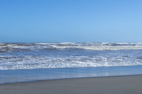 Free Peaceful ocean waves crash onto a sandy beach under a clear blue sky. Stock Photo