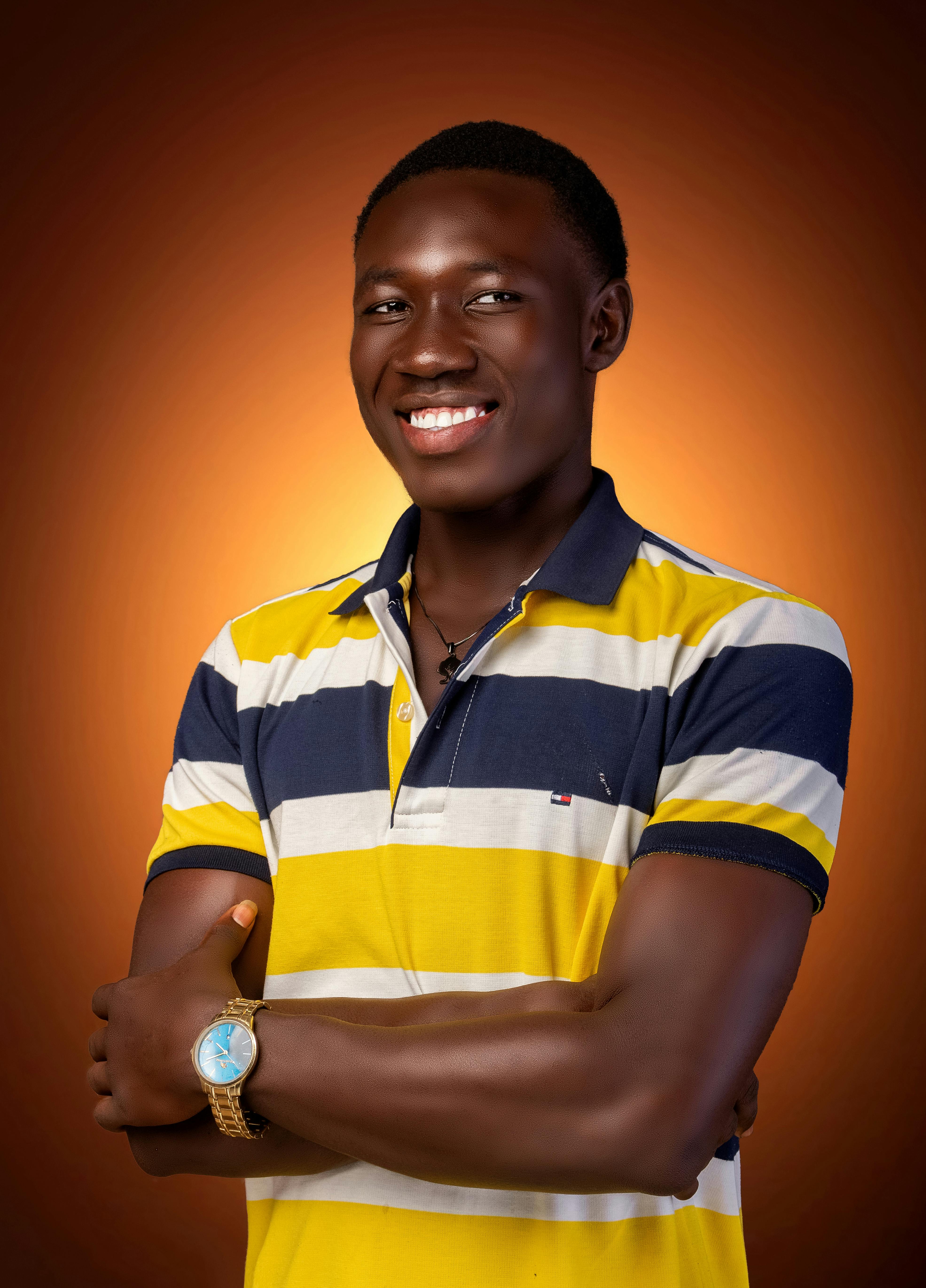 Portrait of a smiling man wearing a yellow striped shirt and watch over an orange background.