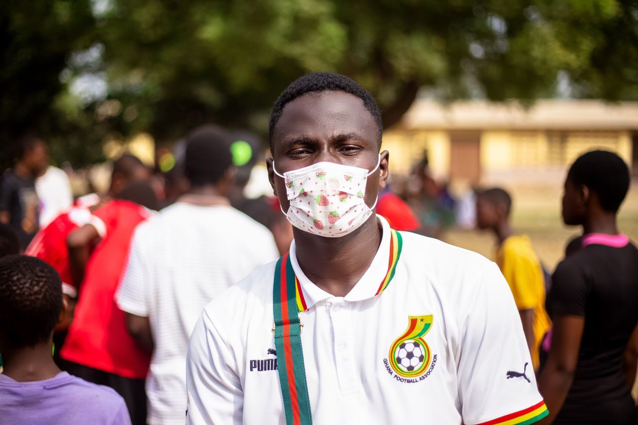 young man wearing a mask at an outdoor event with a vibrant crowd in t