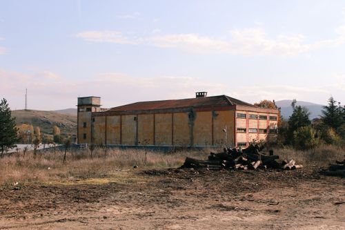 Free Old industrial building in rural landscape with log pile, under clear sky. Stock Photo