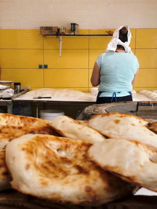 Free Back view of a baker in a cozy bakery preparing fresh naan on a rustic table. Stock Photo