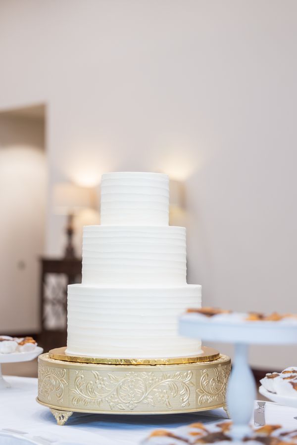 Three-tier white wedding cake on an ornate gold stand