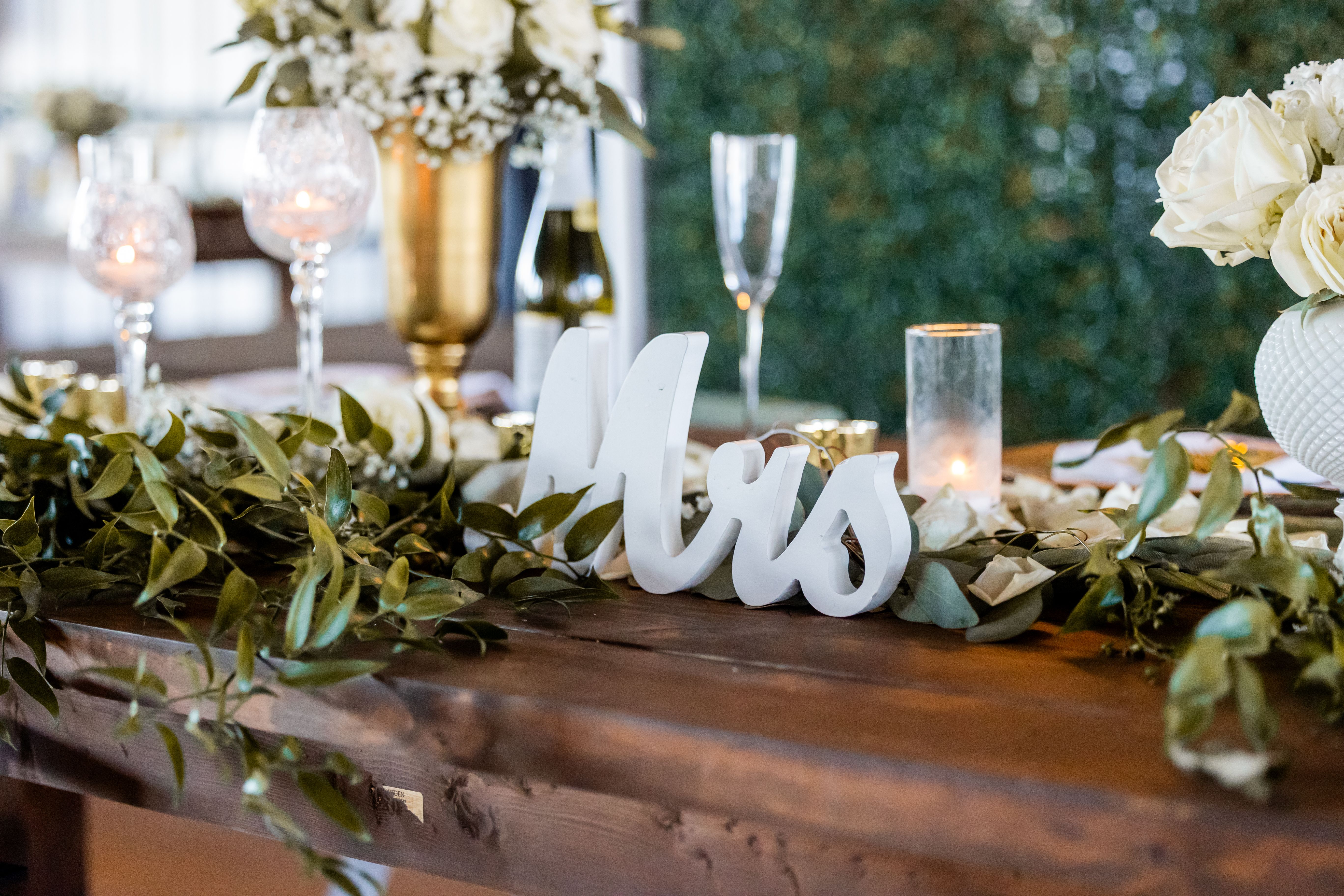 Elegant wedding table setting with white flowers, candles, and 'Mrs' sign for a romantic ambiance.