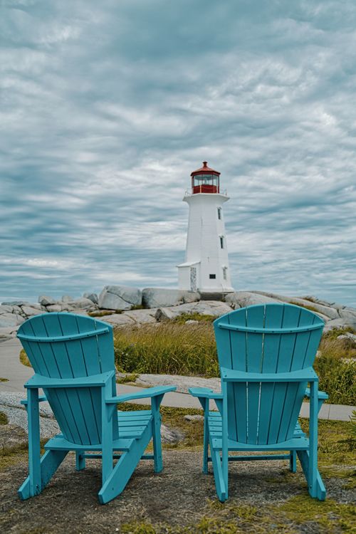 Free Two blue chairs overlooking the iconic Peggys Cove Lighthouse on a cloudy day. Stock Photo