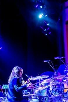 Musician passionately playing drums under colorful stage lights at a live concert.