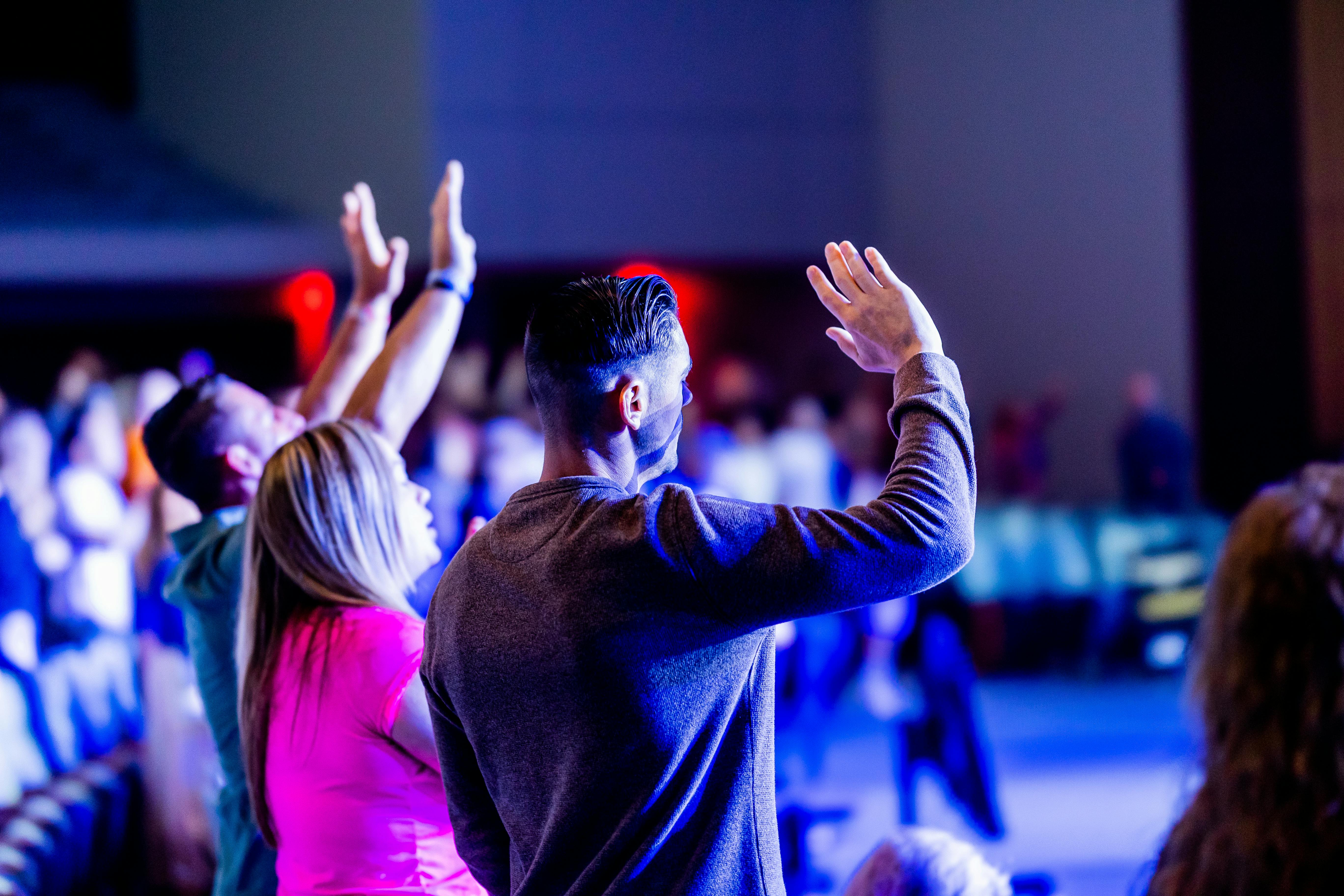 Adults participating in an indoor event, raising hands in engagement. Bright and dynamic atmosphere.