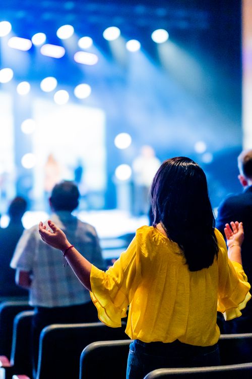 Free A woman in a yellow blouse with hands raised at a lively concert event indoors. Stock Photo