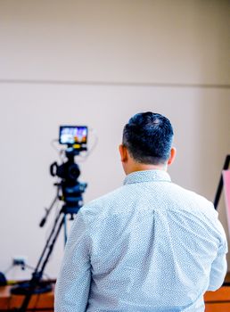A man in a studio setting preparing to operate a camera on a tripod, focused on video production.