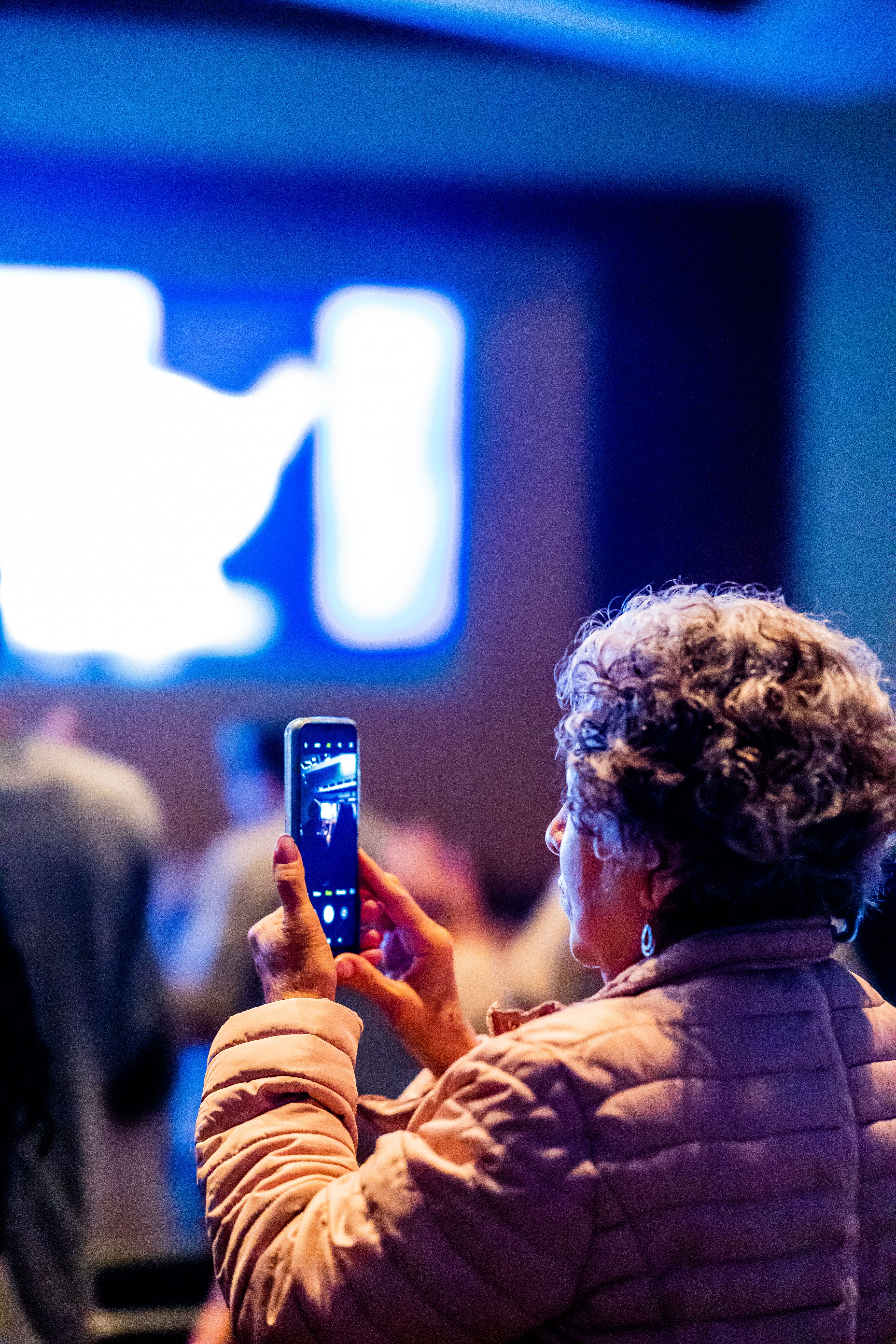A senior woman uses her smartphone to capture a moment at an indoor event.