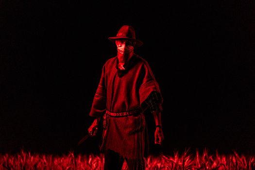 A gaucho stands with a knife, enveloped in dramatic red lighting in a field at night.