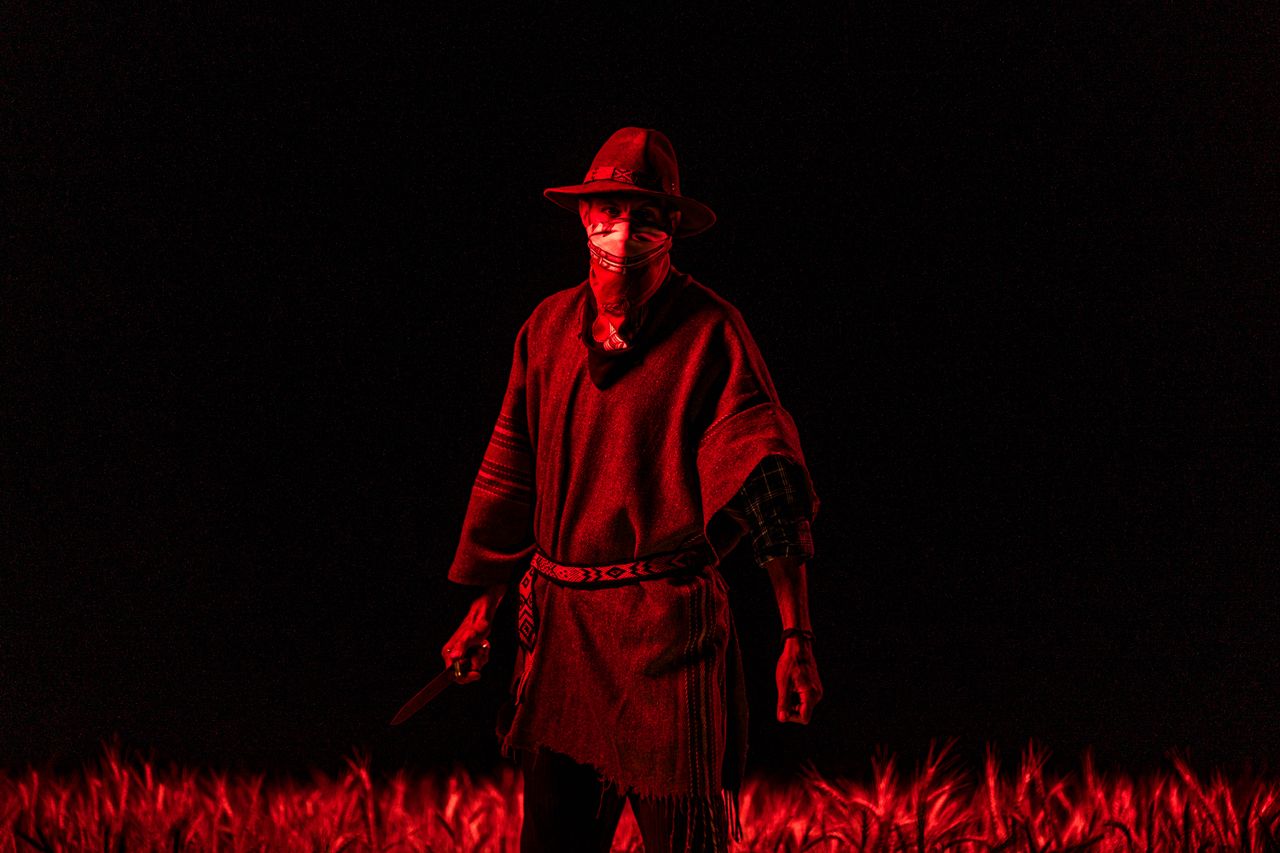 a gaucho stands with a knife enveloped in dramatic red lighting in a f