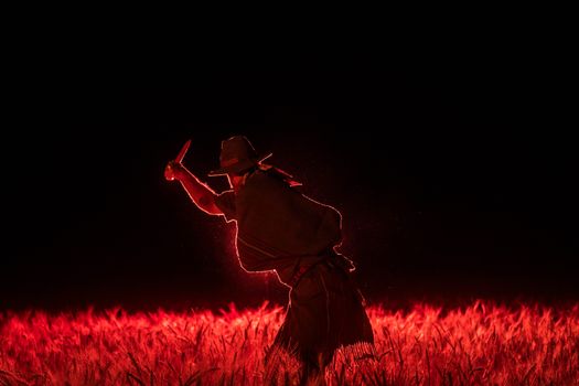 Silhouette of a gaucho holding a knife in a vibrant red wheat field at night in Córdoba, Argentina.