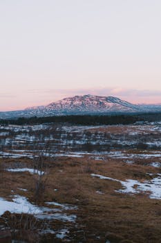 A serene winter landscape featuring a snow-capped mountain during sunrise, showcasing icy and barren wilderness.