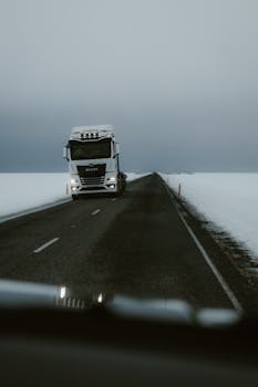White truck on a deserted winter highway surrounded by snow, creating a moody scene.