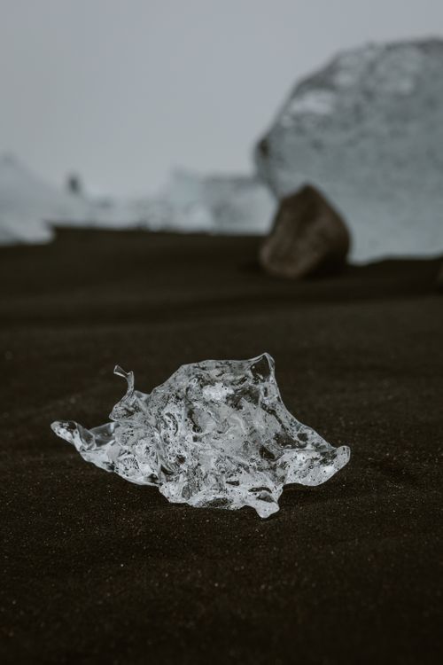 Free A crystalline ice shard rests on dark, volcanic sand, creating a stark contrast in color and texture. Stock Photo