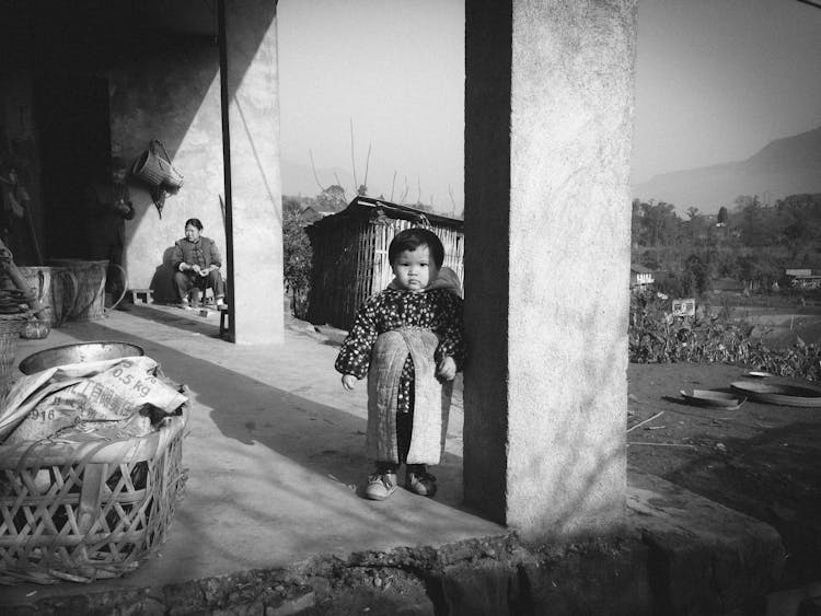 Small Baby Standing On A House Terrace In A Village 