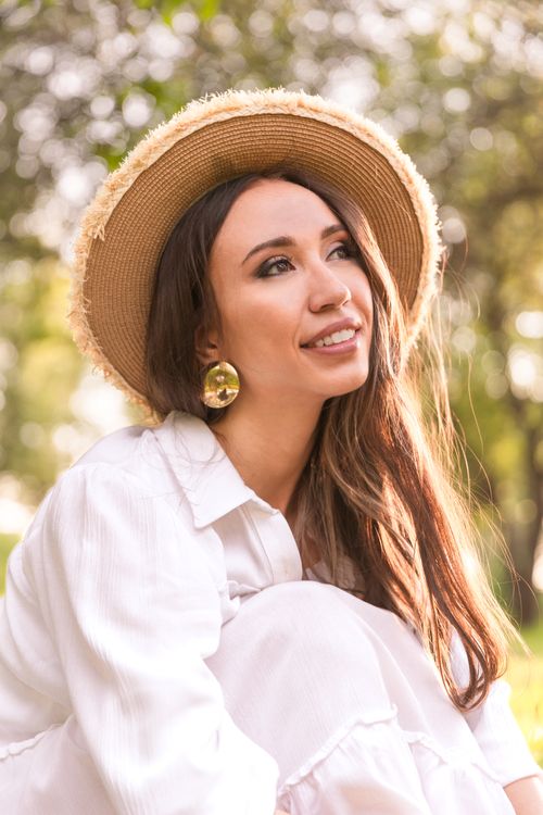 Free Young woman in a straw hat smiling outdoors, surrounded by nature. Stock Photo