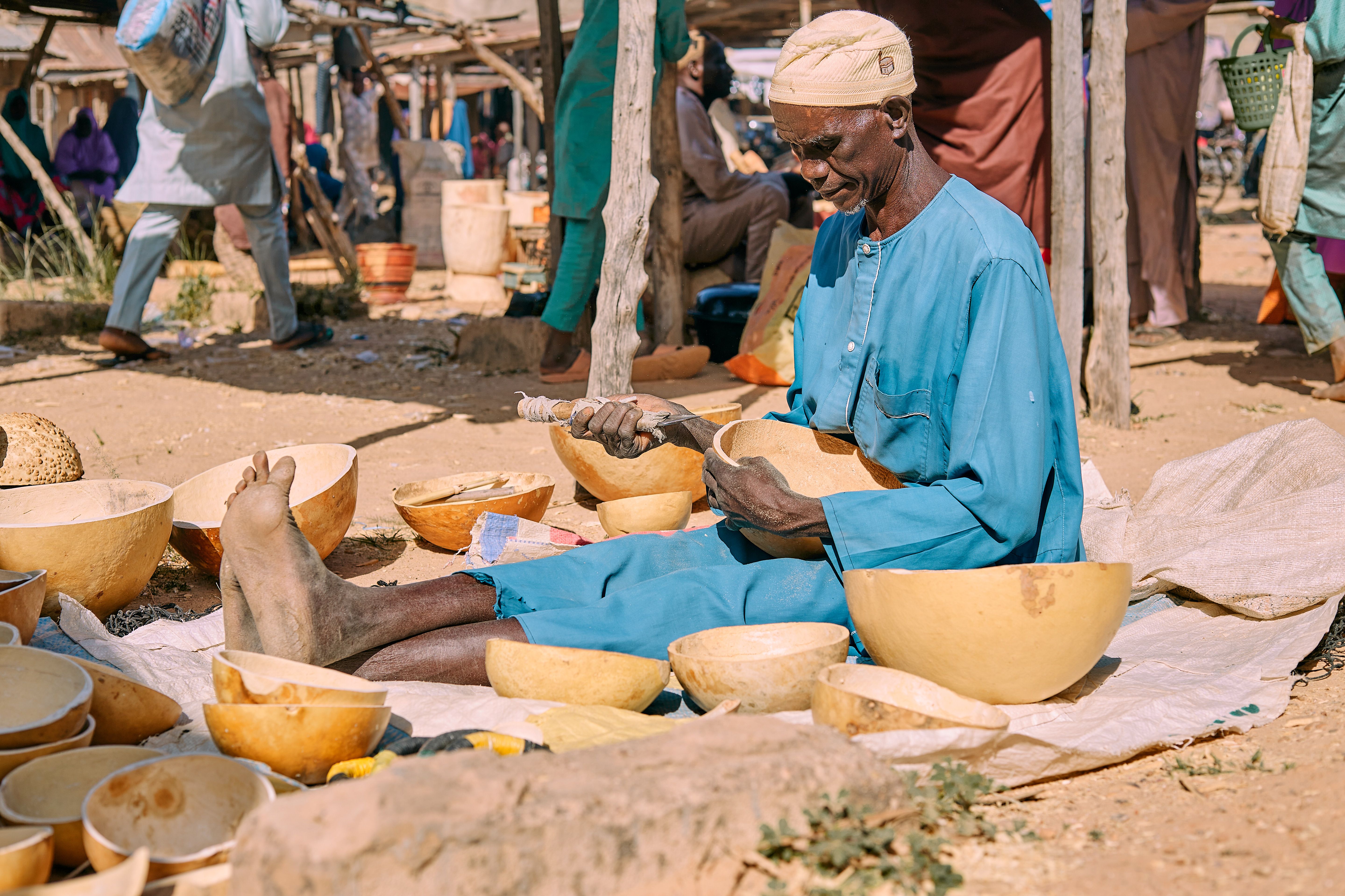 Elderly man crafting bowls in a vibrant outdoor market, highlighting African craftsmanship.