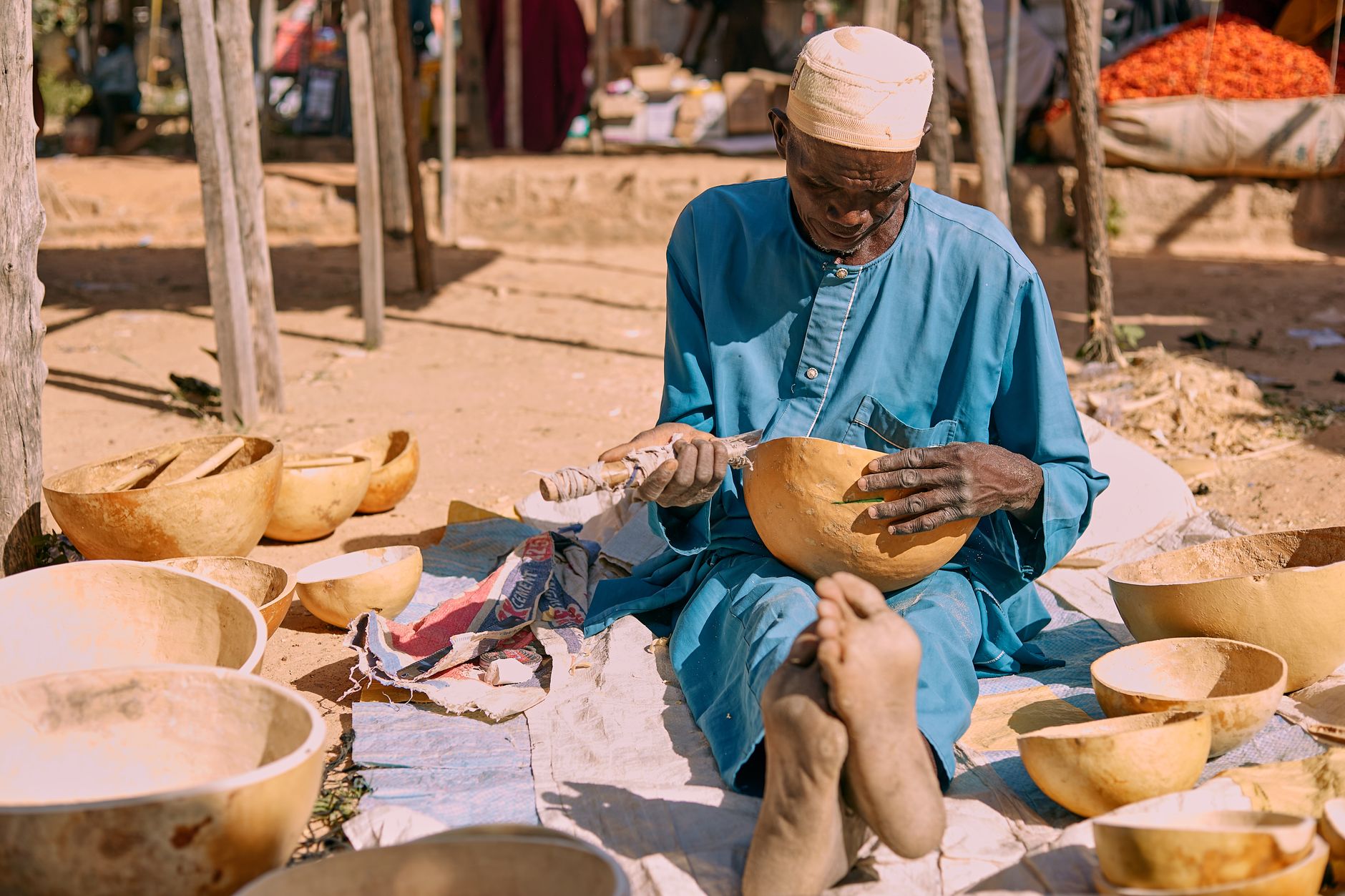 An African man skillfully carves wooden bowls in an outdoor market setting.