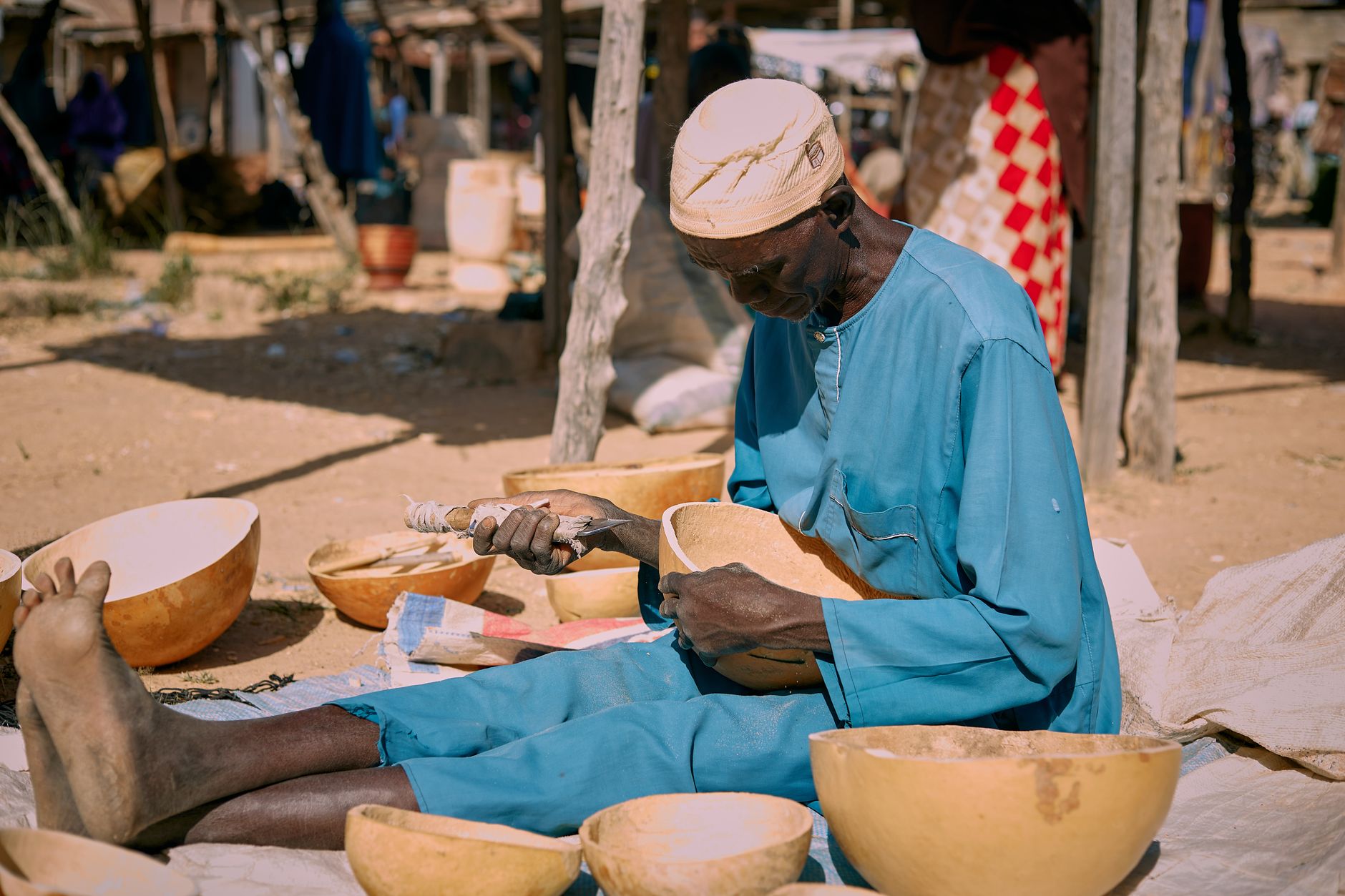 Man in traditional attire handcrafting wooden bowls at an outdoor market.