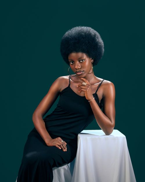 Free Stylish portrait of a woman with afro hairstyle in elegant black outfit against green background. Stock Photo
