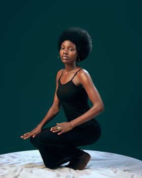 Stylish portrait of an elegant woman kneeling on fabric in a studio setting.