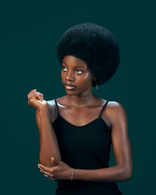 Free Stylish portrait of a young woman with afro hairstyle against a green background, exuding confidence and charm. Stock Photo