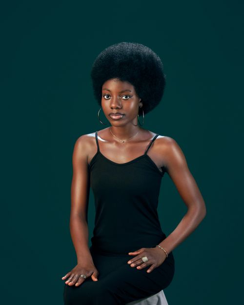 Free Stylish portrait of a woman with an afro, sitting gracefully in a studio setting. Stock Photo