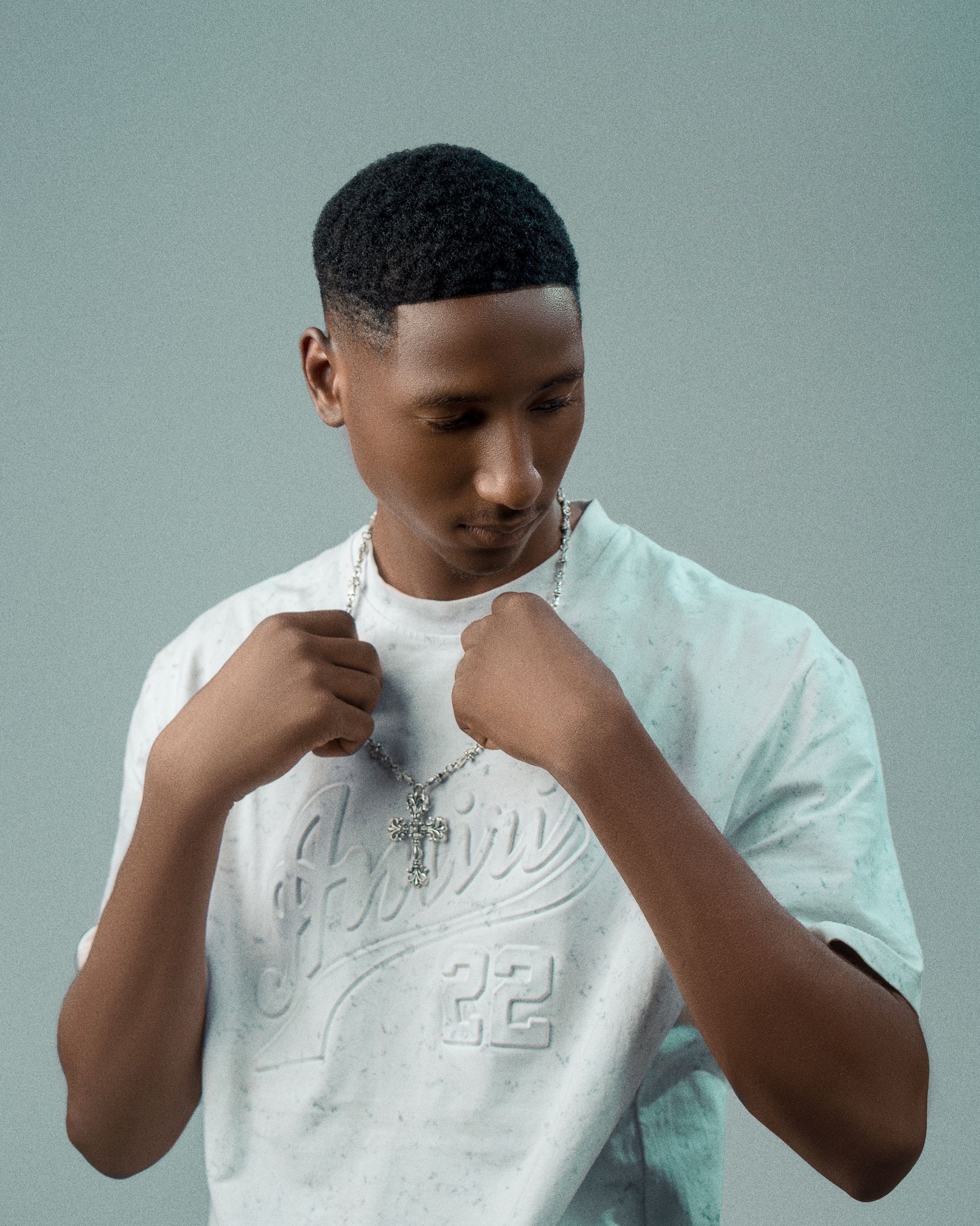 Portrait of a young male posing with a cross necklace in a studio setting.