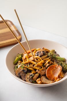 A vibrant dish featuring stir-fry noodles with mushrooms, carrots, and broccoli.