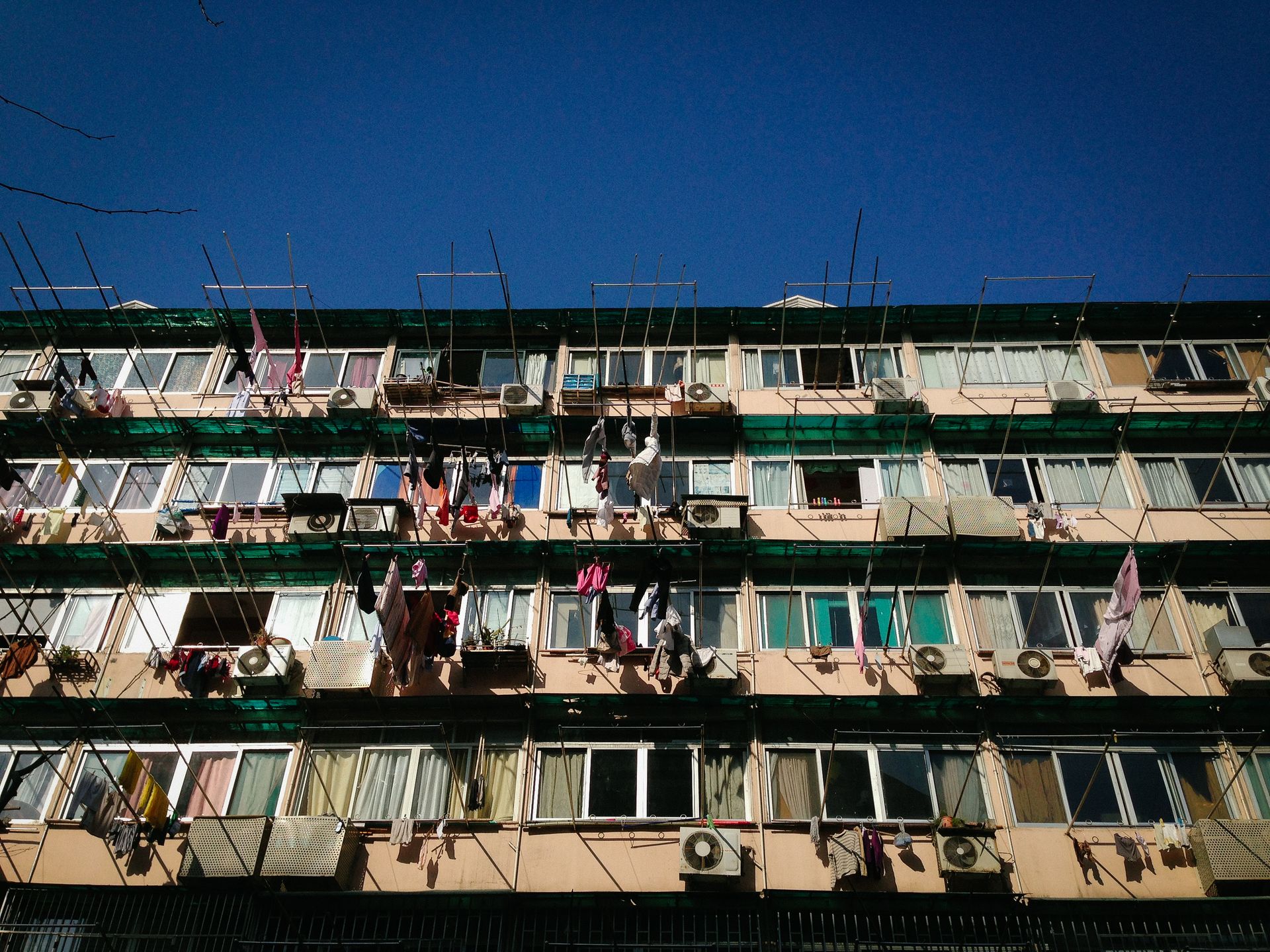 Low-angle view of a residential building with hanging clothes and air conditioners under a clear blue sky.