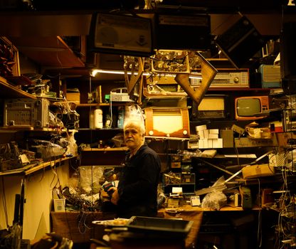 An elderly man in a cluttered workshop with vintage electronics and retro gadgets.