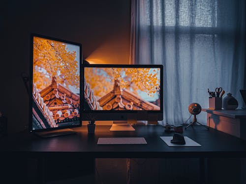 Two Turned-on Flat Screen Computer Monitors on Desk