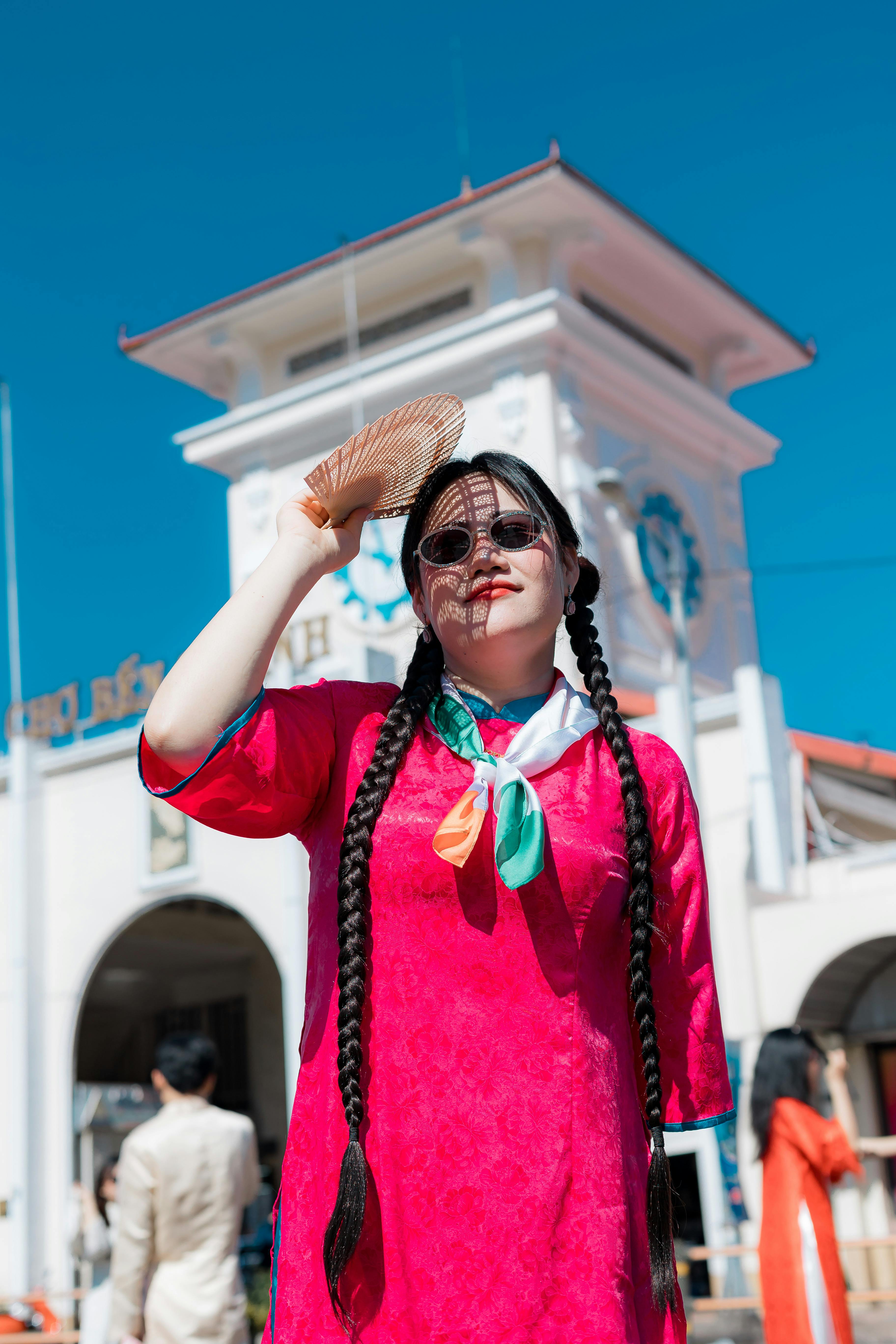 Woman in vibrant traditional attire poses in front of a well-known landmark, basking in sunlight.