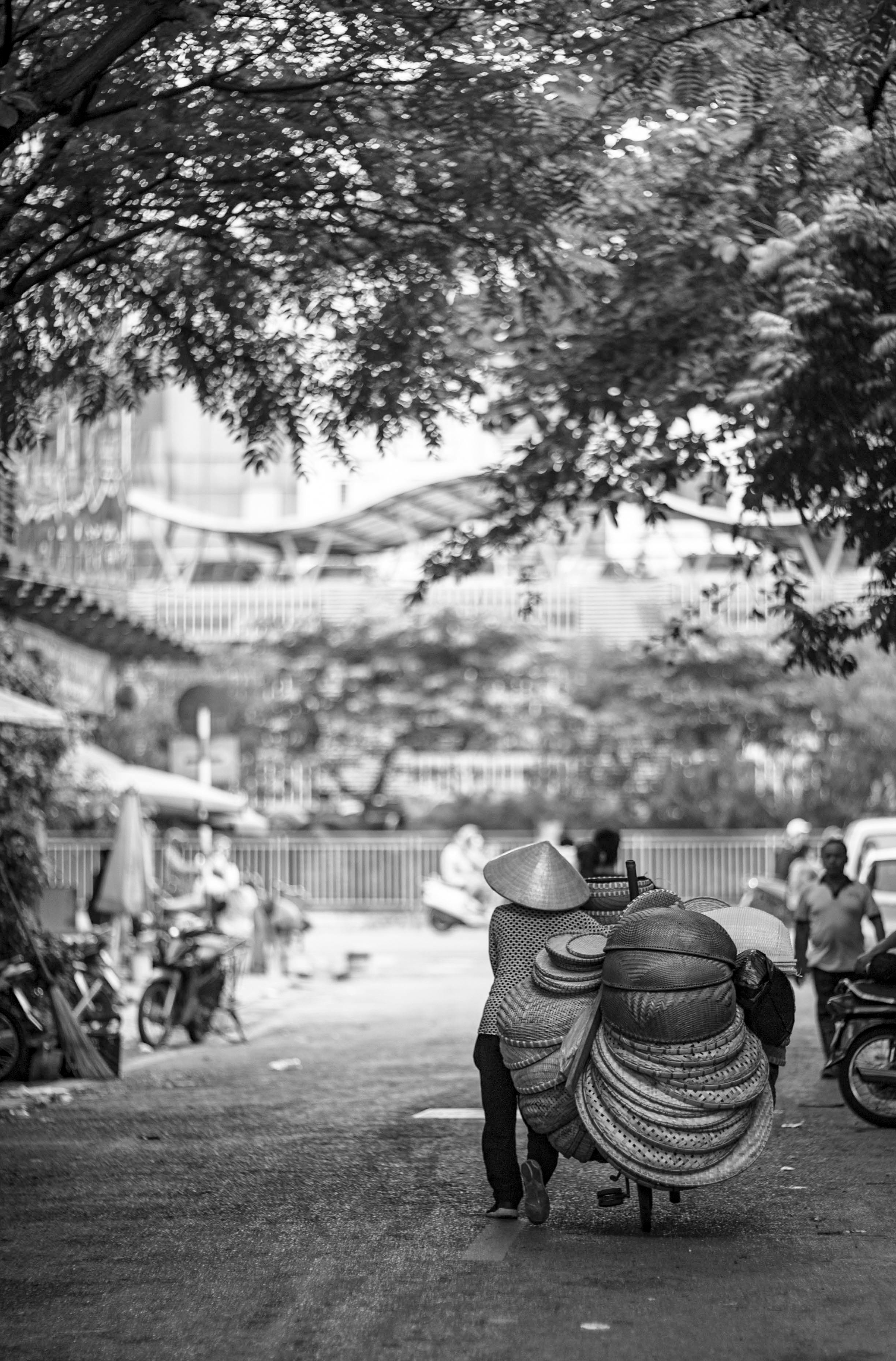 A street vendor pushes a cart filled with woven baskets on a bustling city street.