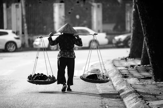 A street vendor in Vietnam walks with a yoke carrying goods in baskets.