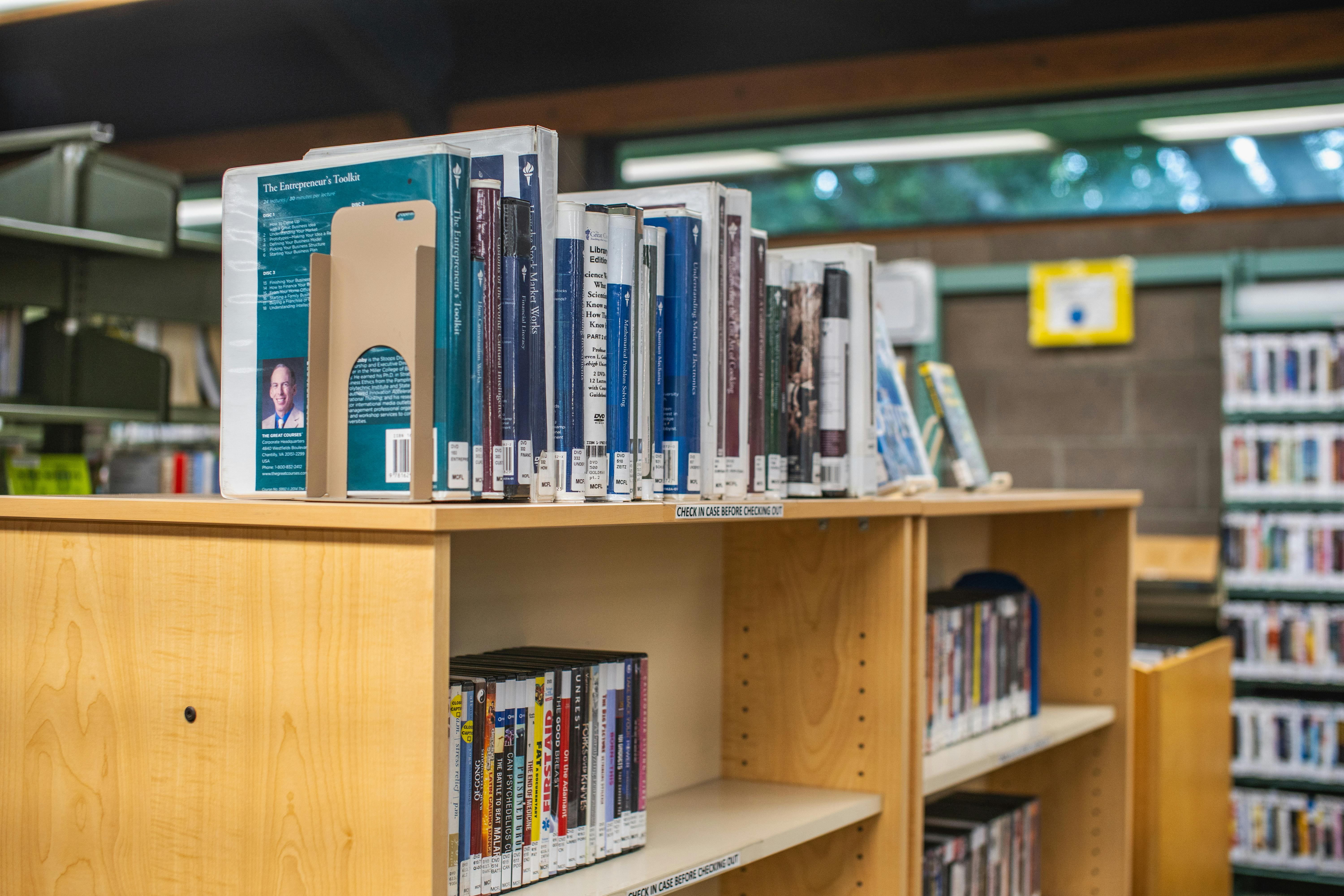 A public library bookshelf displaying a variety of books and DVDs, providing a cozy reading atmosphere.