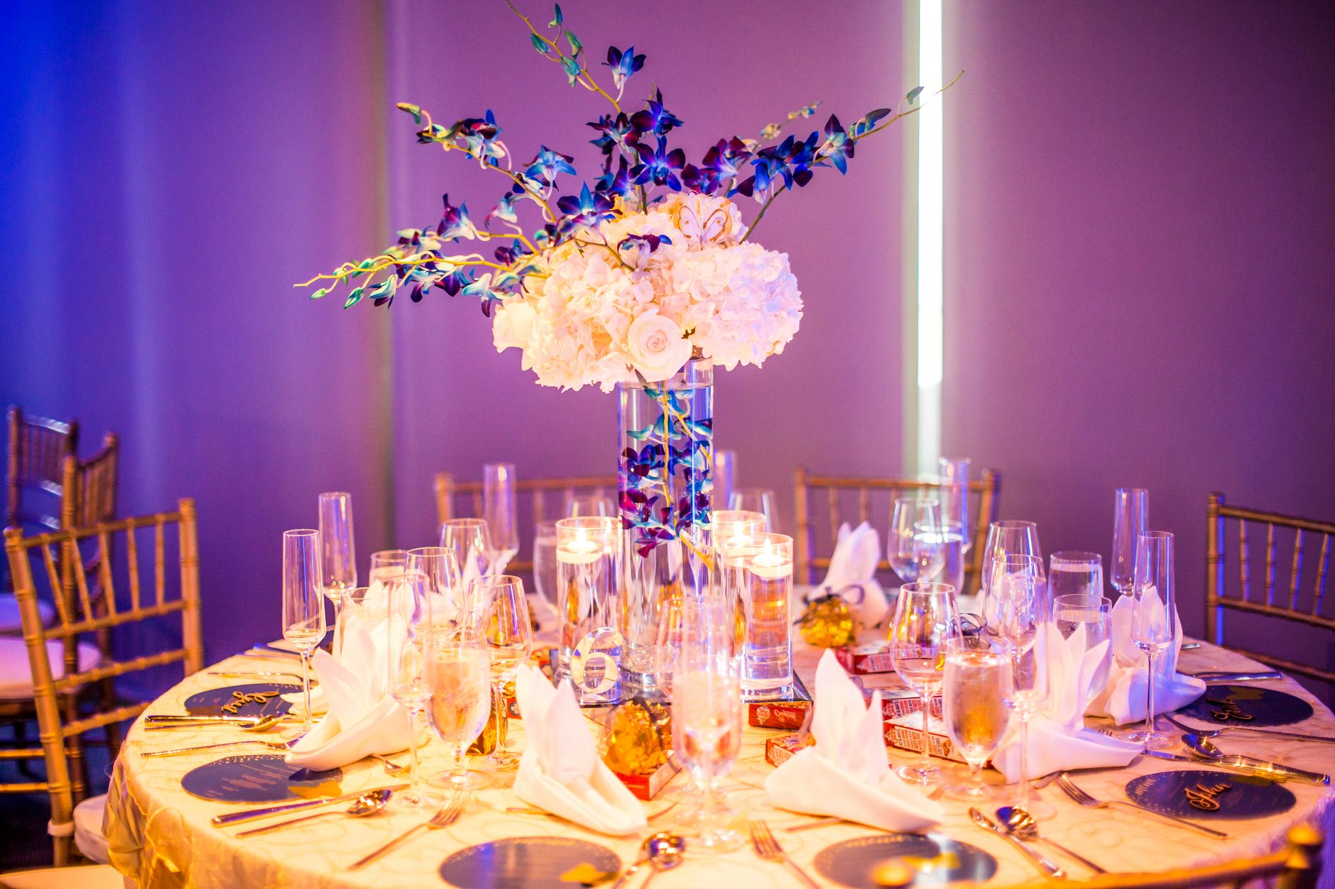 Luxurious wedding table decor featuring white and blue floral centerpiece, candles, and fine dining setup.