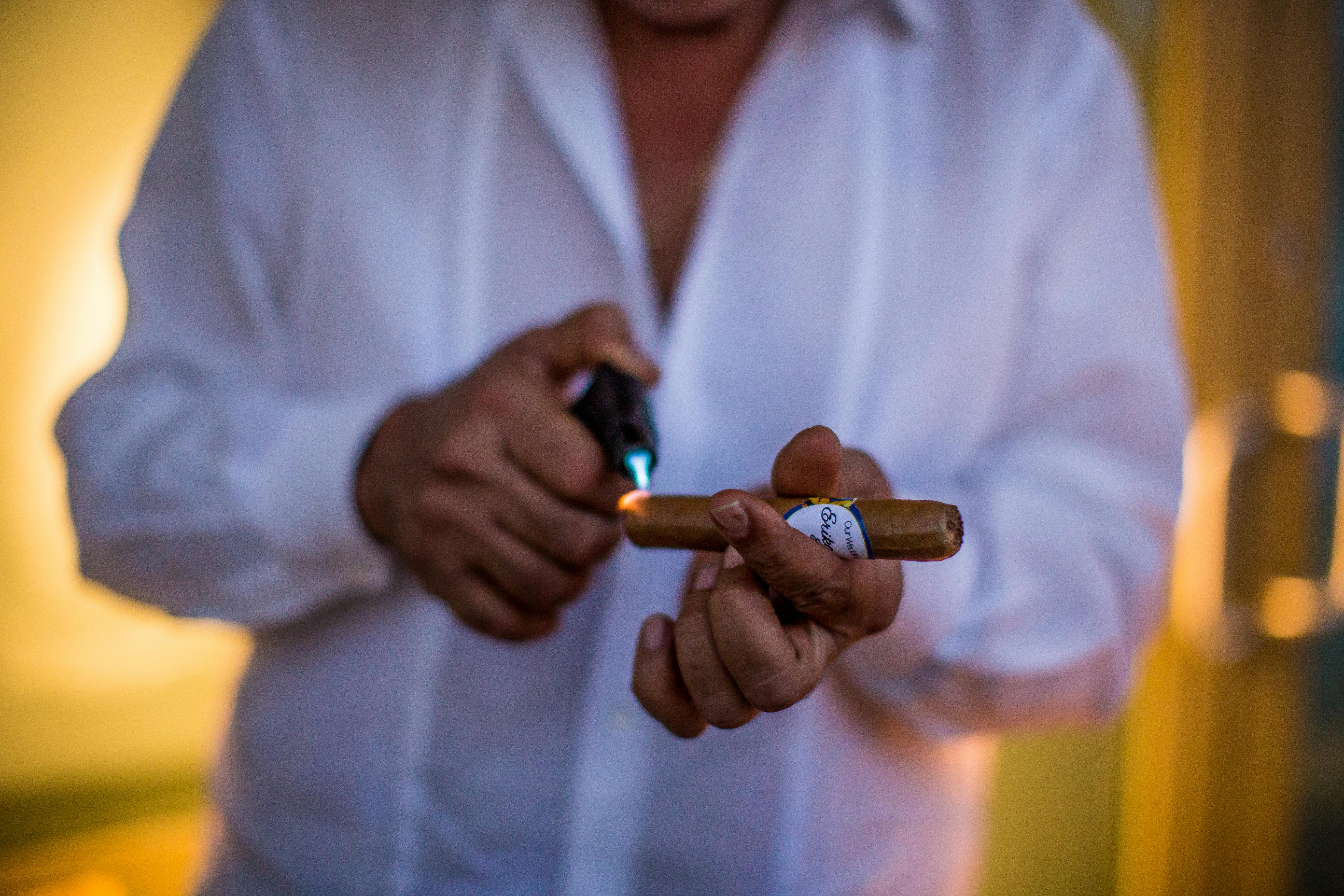 Close-up of a man lighting a cigar with a butane torch, indoors.