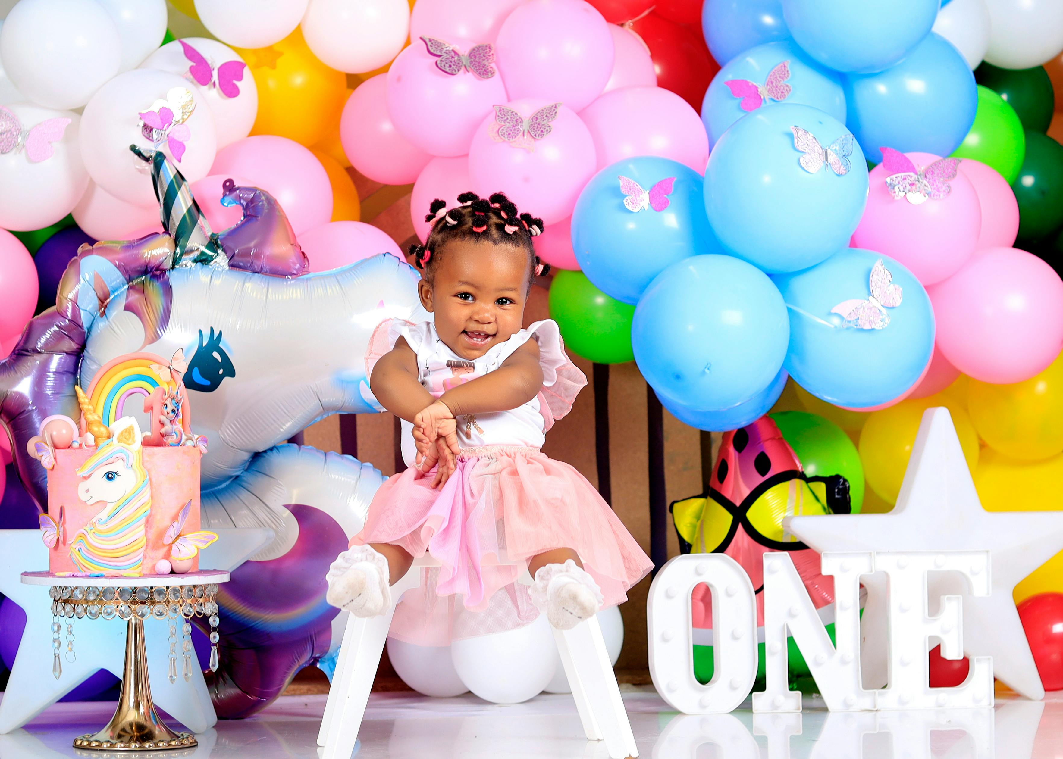 Adorable child at a colorful first birthday party with unicorn theme and balloons.