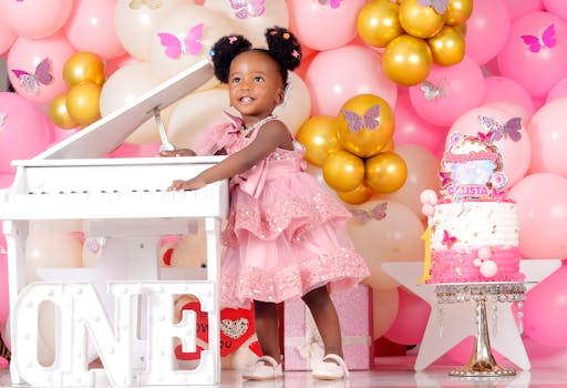 Charming first birthday setup featuring a little girl in a pink dress with festive balloons and cake.