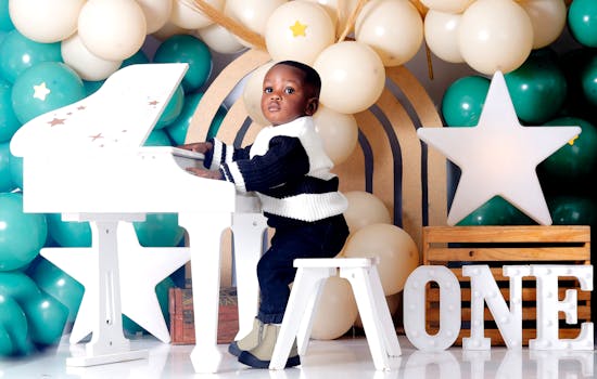 A child enjoying a first birthday celebration with a toy piano and festive balloons.