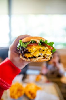 Close-up of a cheeseburger with melted cheese, lettuce, and tomato held in a vibrant setting.